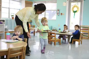 A toddler practicing fine motor skills by threading beads in a Montessori environment.